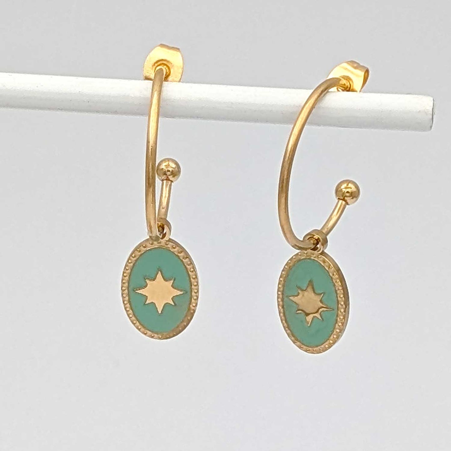 Détail des boucles d'oreilles créoles Sky dorées avec pendentif ovale étoilé vert