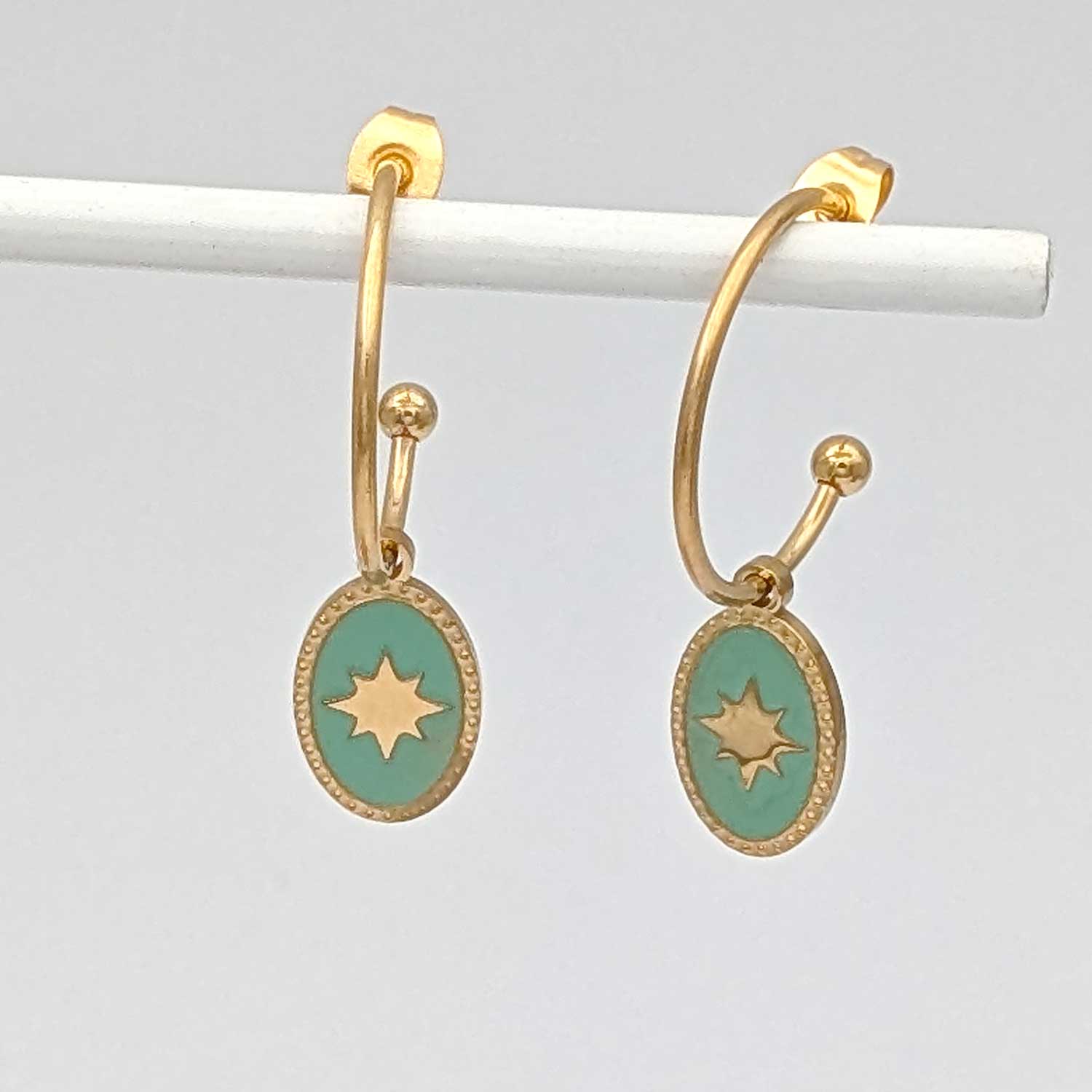 Détail des boucles d'oreilles créoles Sky dorées avec pendentif ovale étoilé vert